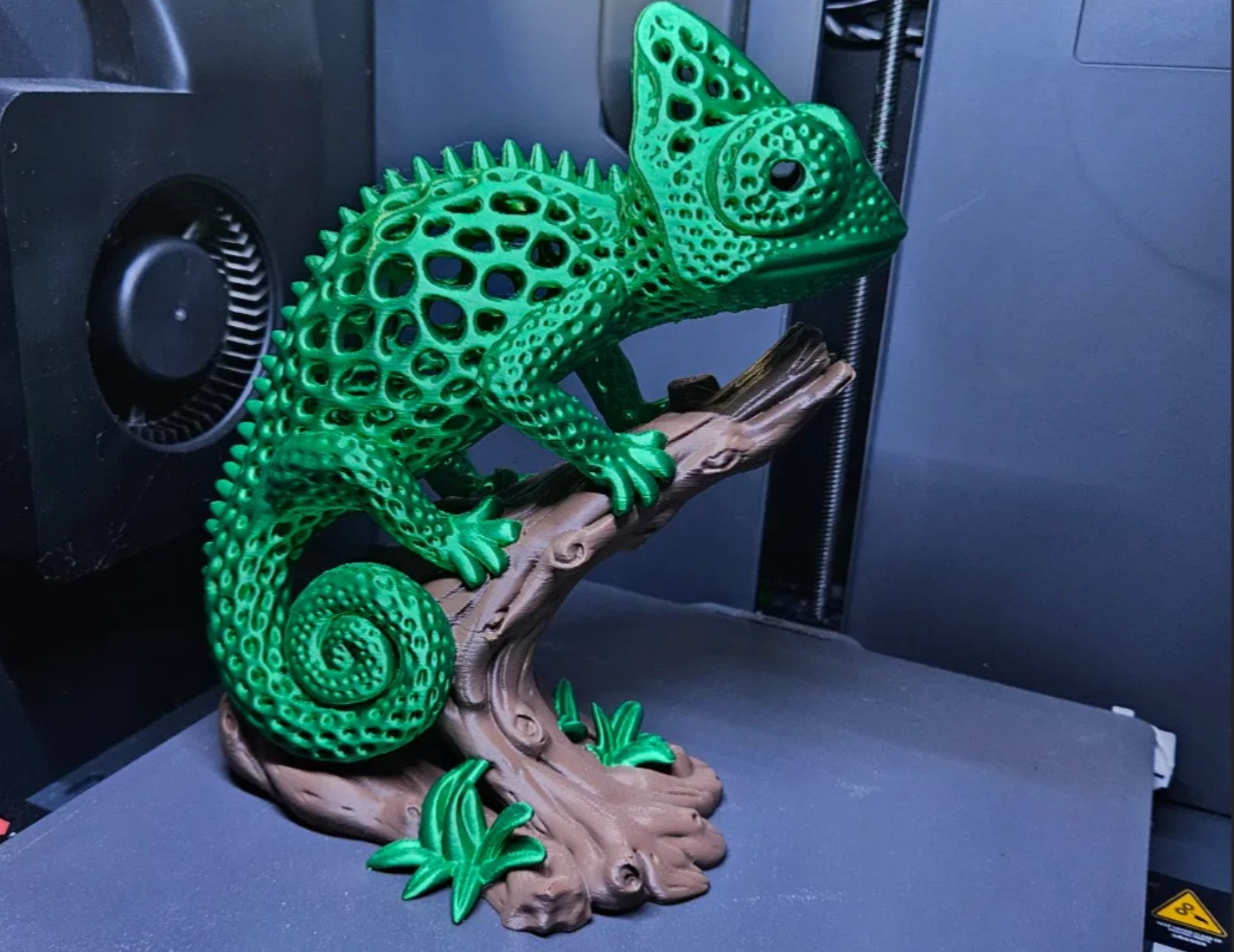 3D printed green voronoi chameleon sculpture on a branch
