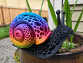 Rainbow Voronoi 3D printed snail sculpture with silk rainbow gradient shell and matte black lattice body on a plant pot