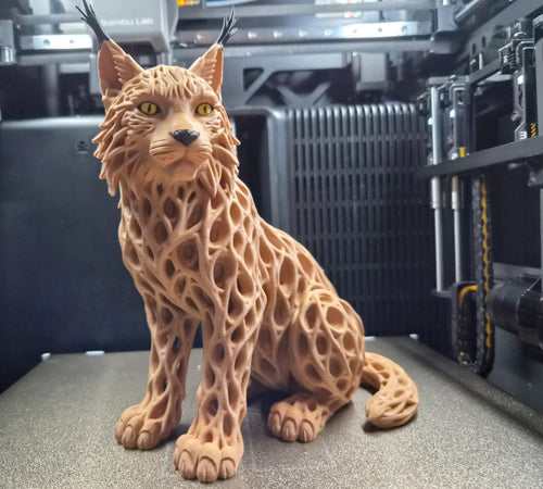 Multi-color 3D printed Voronoi lynx sculpture in tawny caramel with golden eyes and black ear tufts, seated pose